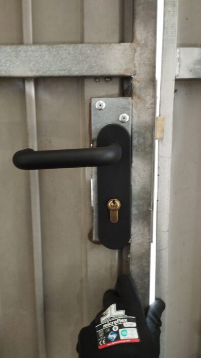 Cerradura con maneta negra y bombín en puerta metálica